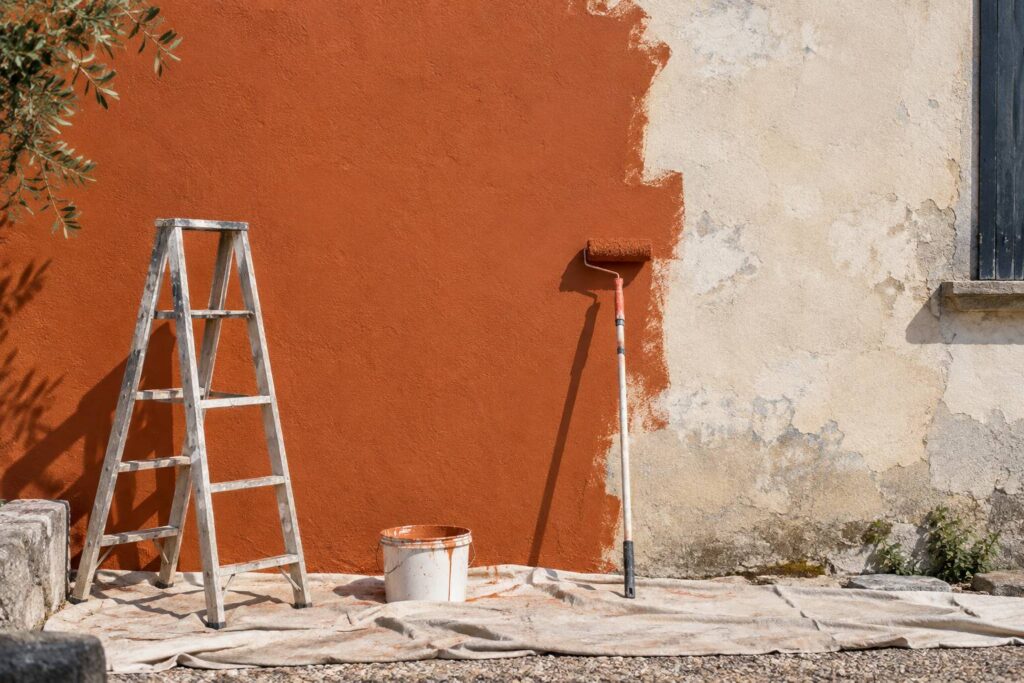 Mur extérieur en cours de peinture avec rouleau, échelle et seau
